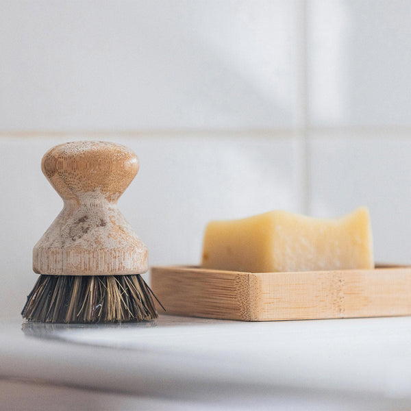 A bar of soap drying on a slatted wooden dish beside a scrub brush
