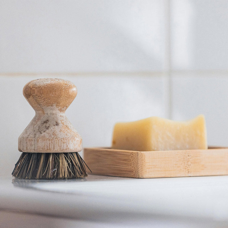 A bar of soap drying on a slatted wooden dish beside a scrub brush